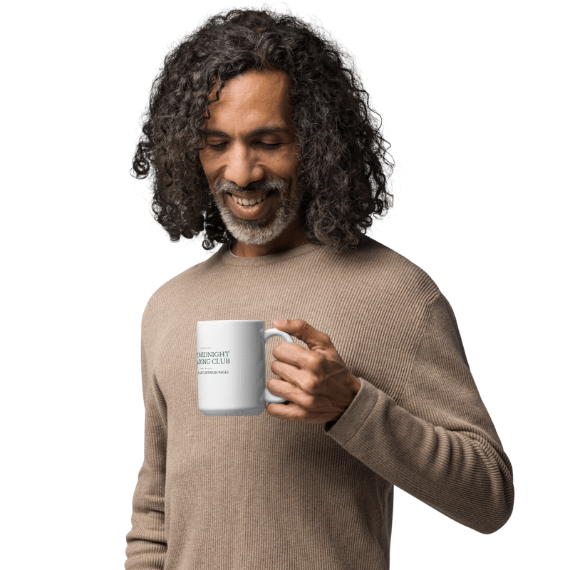 man in a beige sweater holding a white mug printed with the Midnight Reading Club lettering