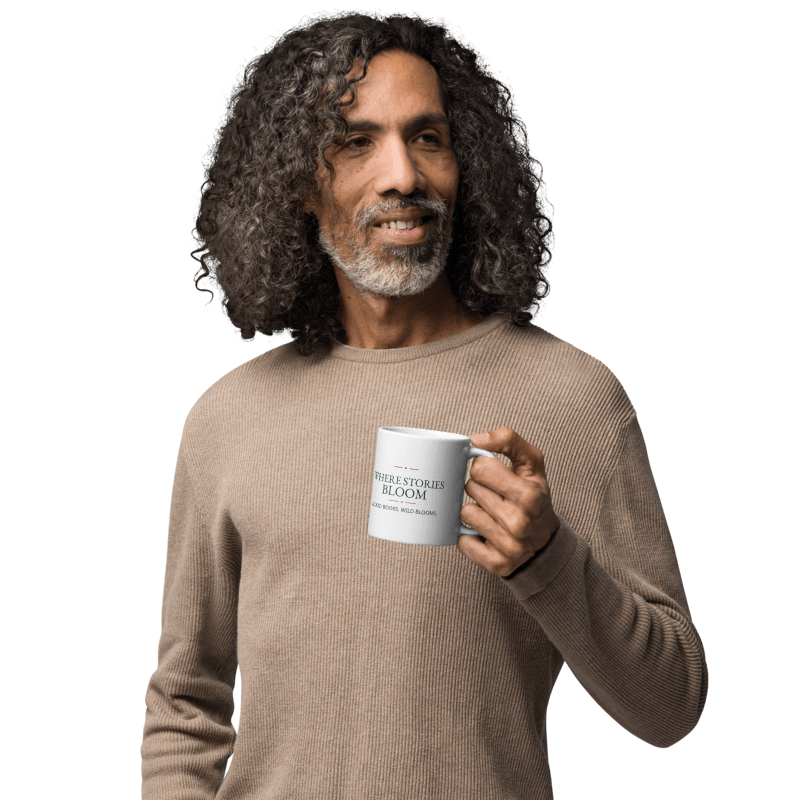 man in a beige sweater holding a white 11 oz mug printed with Where Stories Bloom lettering