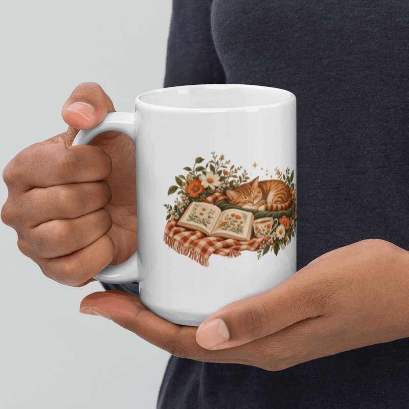hands holding a white ceramic A Sunday Well Read mug with the sleepy cat illustration facing out