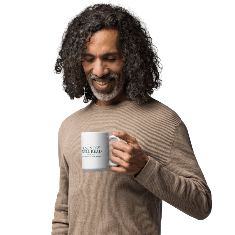 man in a beige sweater holding a white 11 oz mug printed with A Sunday Well Read lettering