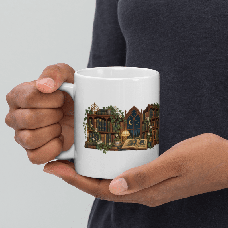 hands holding a white ceramic Lost in Lovely Chapters mug with the library illustration facing out