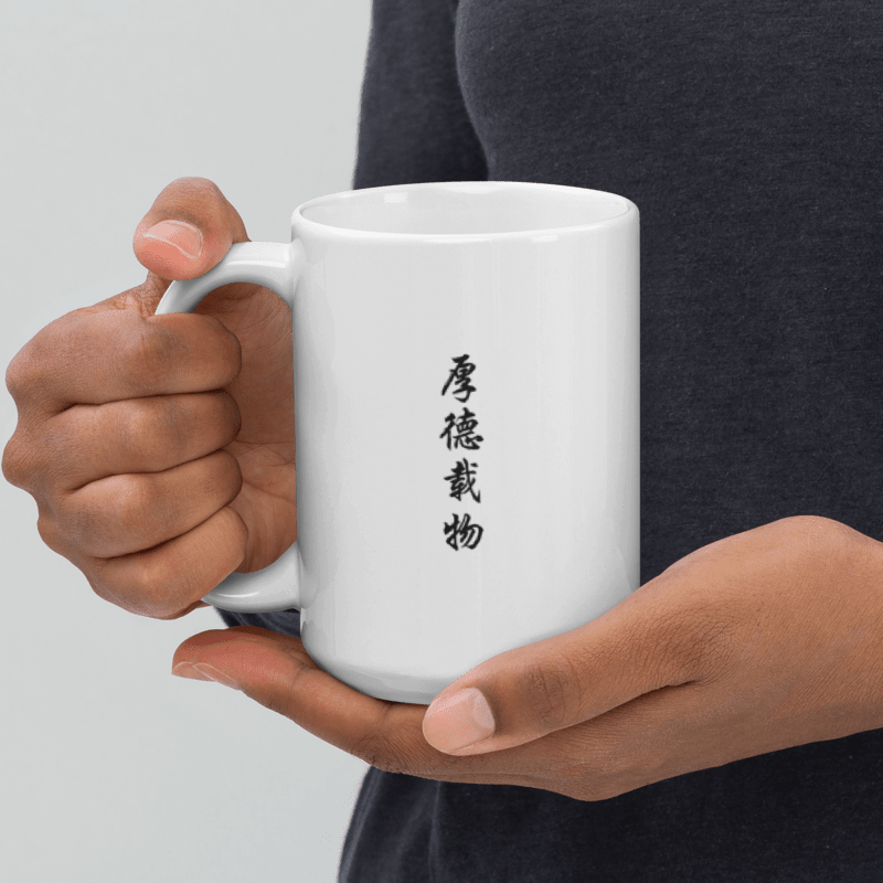 Hand holding a white ceramic mug with the Chinese phrase 厚德载物